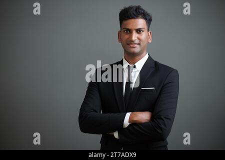 Studio-Porträt eines lächelnden, selbstbewussten jungen Geschäftsmannes im Anzug, der die Arme kreuzt und in die Kamera blickt Stockfoto