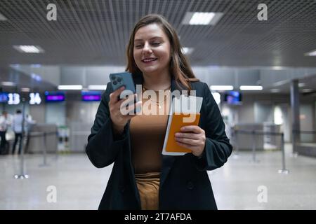 Geschäftsfrau, die sich vom Flughafen aus beeilt, mit einem Pass mit Tickets und einem Koffer beim Telefonieren mit dem Handy im Taxi steht. Unternehmen Stockfoto