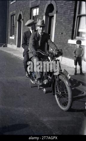 1950er Jahre, historisch, zwei gut gekleidete Gentleman, mit Hüten, auf einem alten Motorrad sitzend, ein Rudge Multi in einer Straße viktorianischer Reihenhäuser, Oldham, Manchester, England, Großbritannien. Der Rudge Multi wurde 1912 von der Rudge-Whitworth Cycle Company hergestellt und war ein riemengetriebenes Motorrad, das 1914 bei den berühmten TT-Rennen auf der Isle of man erfolgreich war, als Cyril Pullin die Tourist Trophy auf einem Rudge Multigear gewann. Stockfoto