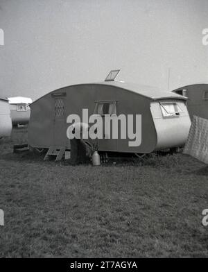 1950er Jahre, historisch, ein junger Mann außerhalb einer Karawane der Ära, 'Oakcroft', mit leeren Bierflaschen und kleinen Milchabfällen, möglicherweise um sie für das Recycling zu sammeln, im Higworth Farm Caravan Camp, Hayling Island, Hampshire, England, Großbritannien. Stockfoto