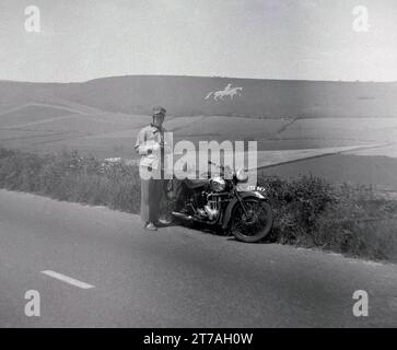 1950er Jahre, historische Motorradtouren, ein männlicher Fahrer, der neben seinem Aerial Motorrad (JYL 947) auf der Straße steht, mit einem Fernglas, um die Landschaft zu genießen, insbesondere das Kreide Osmington White Horse, ein Hügel in Dorset, England, Großbritannien. Das Weiße Pferd stellt König Georg III. Auf seinem Pferd dar. Stockfoto