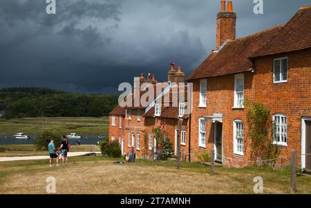 Blick auf Eine Linie von Cottages bei Bucklers Hard in Richtung Beaulieu River mit Einem Sturm im Hintergrund, Beaulieu, Großbritannien Stockfoto