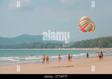 Ein Mann, der mit dem Parasailing fliegt. Die Leute am Strand sehen ihn an. Farbenfroher Fallschirm. PHUKET, THAILAND - 07. APRIL 2023 Stockfoto