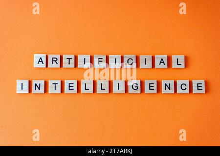 Wort künstliche Intelligenz. Der Begriff AI ist in Holzbuchstaben von oben angeordnet. Orangefarbener flacher Lay-Hintergrund Stockfoto