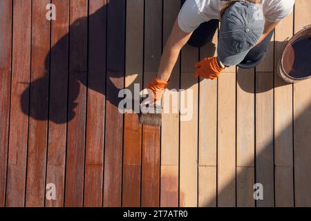 Abdichtung und Färbung von Holzdecks im Außenbereich, Überkopfarbeiter, die Farbe der Schutzdecks auftragen Stockfoto