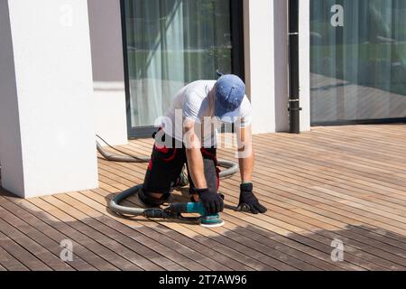 Decksbauer schleifen ipe-Holzbretter mit dem professionellen Schwingschleifer auf der Außenterrasse Stockfoto