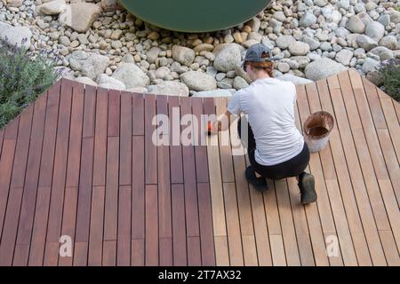 Hartholzdeckenöl-Anwendung, Overhead-Frau, die Holzbretter von Gartendeckungen anstrich Stockfoto