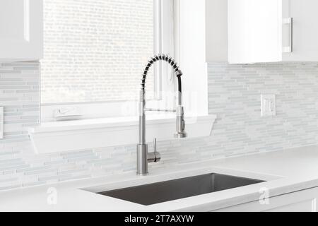 Ein Küchenarmatur mit poliertem Edelstahl-Wasserhahn, einem Glas- und Steinmosaikfliesen und weißen Schränken. Stockfoto