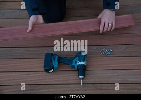 Elektrischer Schraubendreher auf Terrassendielen, Hände des Deckschreiners halten ipe-Holzbrettholz Stockfoto