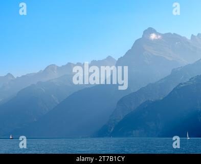 Umrisse der Berge am schweizer Urnersee im tagsüber trüben Licht. Segelboote auf dem See Stockfoto