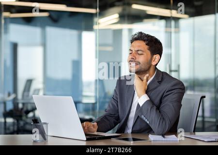 Junger Mann hat eine Halsschmerzen während der Arbeit im Büro, Geschäftsmann hat gesundheitliche Probleme, Husten virale Krankheit Halsschmerzen, Gesundheitskonzept. Stockfoto