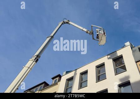 Unteransicht der Kabine und des Auslegers eines hydraulischen Lifts über einem weißen Gebäude vor einem Hintergrund des blauen Himmels mit hellen Wolken. Stockfoto