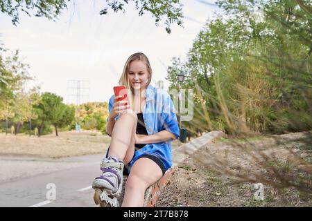 Sportliche Frau auf Inline-Skates, die auf dem Smartphone plaudert. Stockfoto