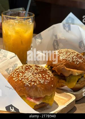 Ein Holztisch in einem Café im Freien mit zwei Cheeseburgern und zwei Getränken Stockfoto