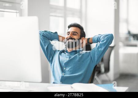 Entspannter indischer Geschäftsmann, der bei der Arbeit Pause macht Stockfoto