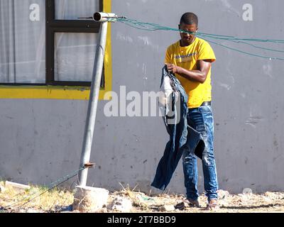 Ein afrikanischer Mann, der seine Jeans vor seinem einfachen Haus in einem Township in Südafrika ausklagert Stockfoto