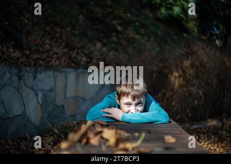 Porträt eines Jungen, der sich auf den Armen auf einem Tisch in einem herbstlichen Park in Georgia stützt Stockfoto