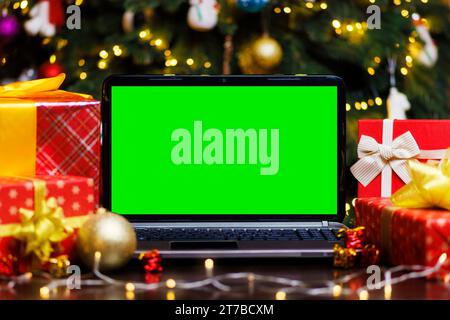 Laptop-Computer mit grünem leerem Bildschirm auf dem Tisch mit Geschenken und Girlande Stockfoto