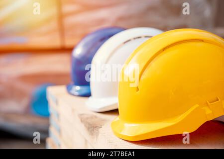 Drei Helme in verschiedenen Farben auf dem Holzbrett Nahaufnahme mit selektivem Fokus. Tragen Sie beim Bau immer persönliche und sichere Schutzausrüstung Stockfoto