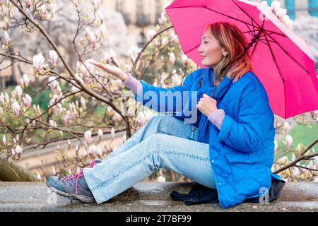 Asiatische Frau im blauen Mantel, die am Frühlingstag in einem Park zwischen Blumen spaziert Stockfoto