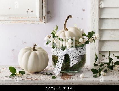 Handgefertigte Herbstdekoration mit kleinen weißen Kürbissen und Schneebarnzweigen im Glasgefäß. Kopierbereich. Das floristische Konzept. Stockfoto