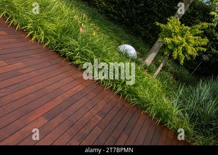 Hölzerne braune Terrassendielen ipe Textur und Gartengrün mit immergrünem Ziergras auf Hintergrund Stockfoto