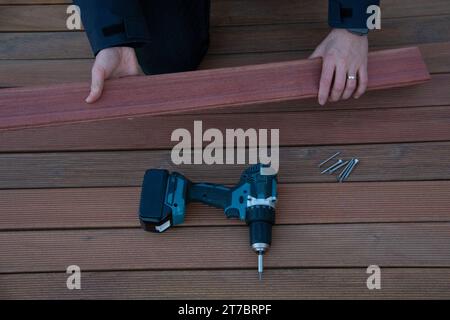 Elektrischer Schraubendreher auf Terrassendielen, Hände des Deckschreiners halten ipe-Holzbrettholz Stockfoto