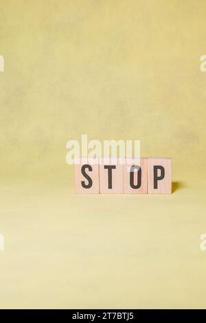 STOPPWORT aus Holzbuchstaben auf gelbem Hintergrund mit Kopierraum für ein Werbekonzept Stockfoto