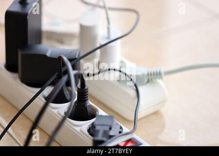 Überlastete Stromversorgungsplatinen. Steckdosenleisten mit verschiedenen Steckern auf weißem Boden. Konzept der Gefahr Gefahr Überlaststrom elektrisch Stockfoto