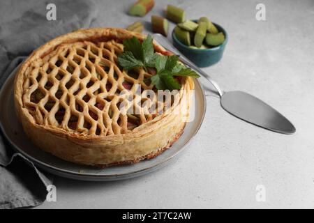 Frisch gebackener Rhabarberkuchen, geschnittene Stiele und Tortenheber auf hellgrauem Tisch Stockfoto