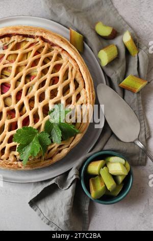 Frisch gebackener Rhabarberkuchen, geschnittene Stängel und Kuchenservice auf hellgrauem Tisch, flach liegend Stockfoto