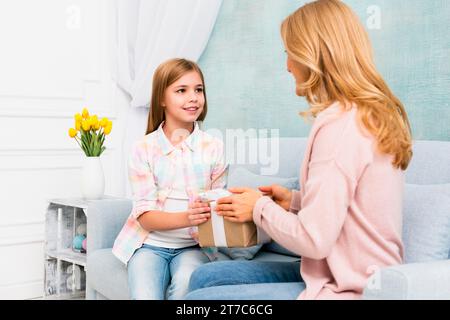 Tochter gibt Geschenkbox und Mutter sitzt auf der Couch Stockfoto