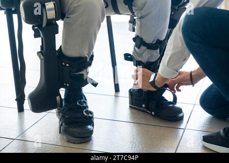 Mechanisches Exoskelett, Physiotherapeut, der die Bänder an den Beinen des behinderten Menschen platziert, um sein Roboterskelett zu platzieren, Physiotherapie in einer modernen Stockfoto