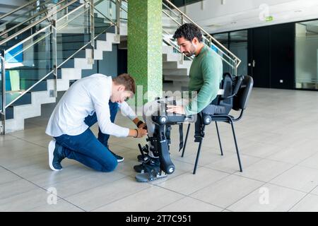 Mechanisches Exoskelett. Physiotherapie in einem modernen Krankenhaus: Physiotherapeut, der die Bänder auf die Knie eines behinderten Menschen legt, um seine zu platzieren Stockfoto