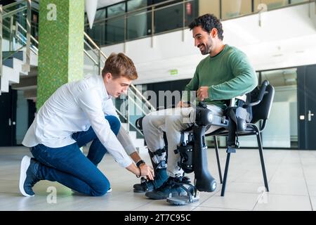 Mechanisches Exoskelett, Physiotherapeut, der die Bänder auf die Knie des behinderten Menschen legt, um sein Roboterskelett zu platzieren, Physiotherapie in A Stockfoto