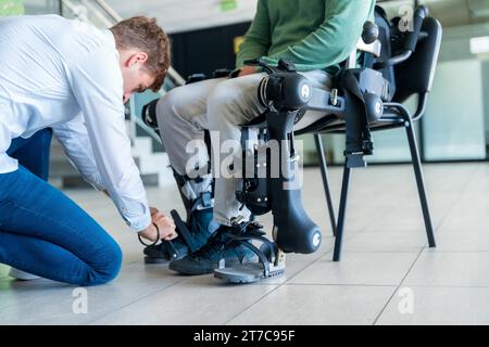 Mechanisches Exoskelett. Physiotherapie in einem modernen Krankenhaus: Physiotherapeut, der die Bänder auf die Knie eines behinderten Menschen legt, um seine zu platzieren Stockfoto