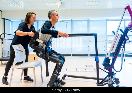 Mechanisches Exoskelett. Physiotherapeutische Assistentin, die einen behinderten Menschen mit Roboterskelett zum Aufstehen bringt. Futuristische Rehabilitation Stockfoto