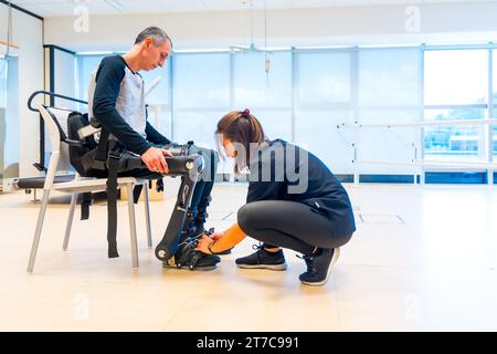 Mechanisches Exoskelett. Physiotherapie in einem modernen Krankenhaus: Physiotherapeutin mit Klebeband auf Behinderte mit Roboterskelett. Futuristisch Stockfoto