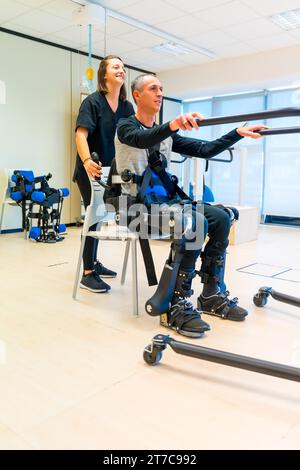 Mechanisches Exoskelett. Weibliche Physiotherapie-Arzthelferin, die behinderte Person mit Roboterskelett zum Aufstehen hebt. Futuristische Rehabilitation Stockfoto