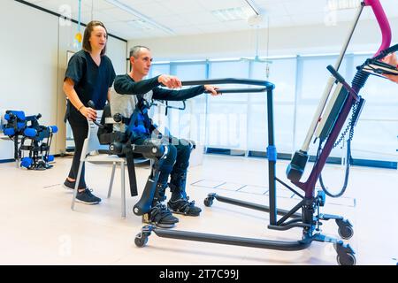 Mechanisches Exoskelett. Weibliche Physiotherapie-Arzthelferin, die behinderte Person mit Roboterskelett zum Aufstehen hebt. Futuristische Rehabilitation Stockfoto