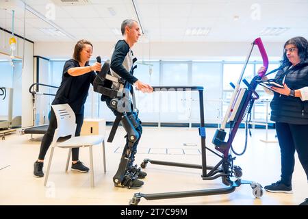 Mechanisches Exoskelett. Physiotherapeutische Assistentin, die einen behinderten Menschen mit Roboterskelett zum Aufstehen bringt. Futuristische Rehabilitation Stockfoto