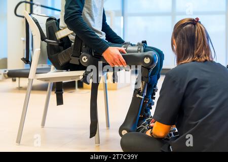 Mechanisches Exoskelett. Physiotherapie in einem modernen Krankenhaus: Physiotherapeutin mit Klebeband auf Behinderte mit Roboterskelett. Futuristisch Stockfoto