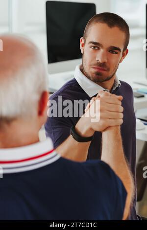 Ein junger Mann in einem Marinepolo strahlt Selbstvertrauen aus, während er mit einem Ältesten im Job einen Handschlag ausübt Stockfoto