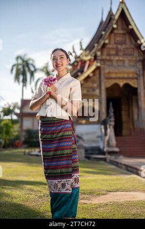 Eine wunderschöne Thai-Frau in einem traditionellen Thai-Lanna-Kleid mit einer Girlande legt ihre Hände in einer Gebetsposition zusammen, während sie vor ihr steht Stockfoto