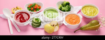 Baby-Püree aus Gemüse und Obst in weißen Schüsseln mit Zutaten auf rosa Hintergrund. Babynahrungskonzept. Draufsicht. Panorama. Stockfoto