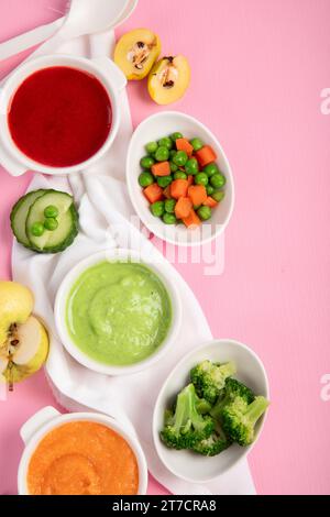 Baby-Püree aus Gemüse und Obst in weißen Schüsseln mit Zutaten auf rosa Hintergrund. Babynahrungskonzept. Draufsicht. Stockfoto