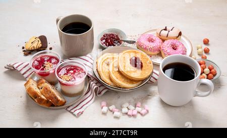 Tisch mit verschiedenen amerikanischen Keksen, Donuts, Pfannkuchen und Kaffeetassen auf weißem Hintergrund. Draufsicht. Stockfoto