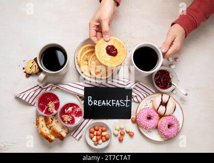 Tisch mit verschiedenen amerikanischen Keksen, Donuts, Pfannkuchen und Kaffeetassen auf weißem Hintergrund. Draufsicht. Stockfoto