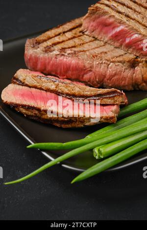 Nahaufnahme gegrillter Rindersteaks mit drei Spitzen, mittelselten mit frischem Gemüse auf schwarzem Hintergrund Stockfoto