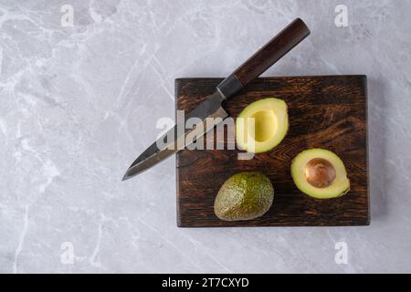 Blick von oben auf ganze und halbe Avocado auf hölzernem Schneidebrett Stockfoto